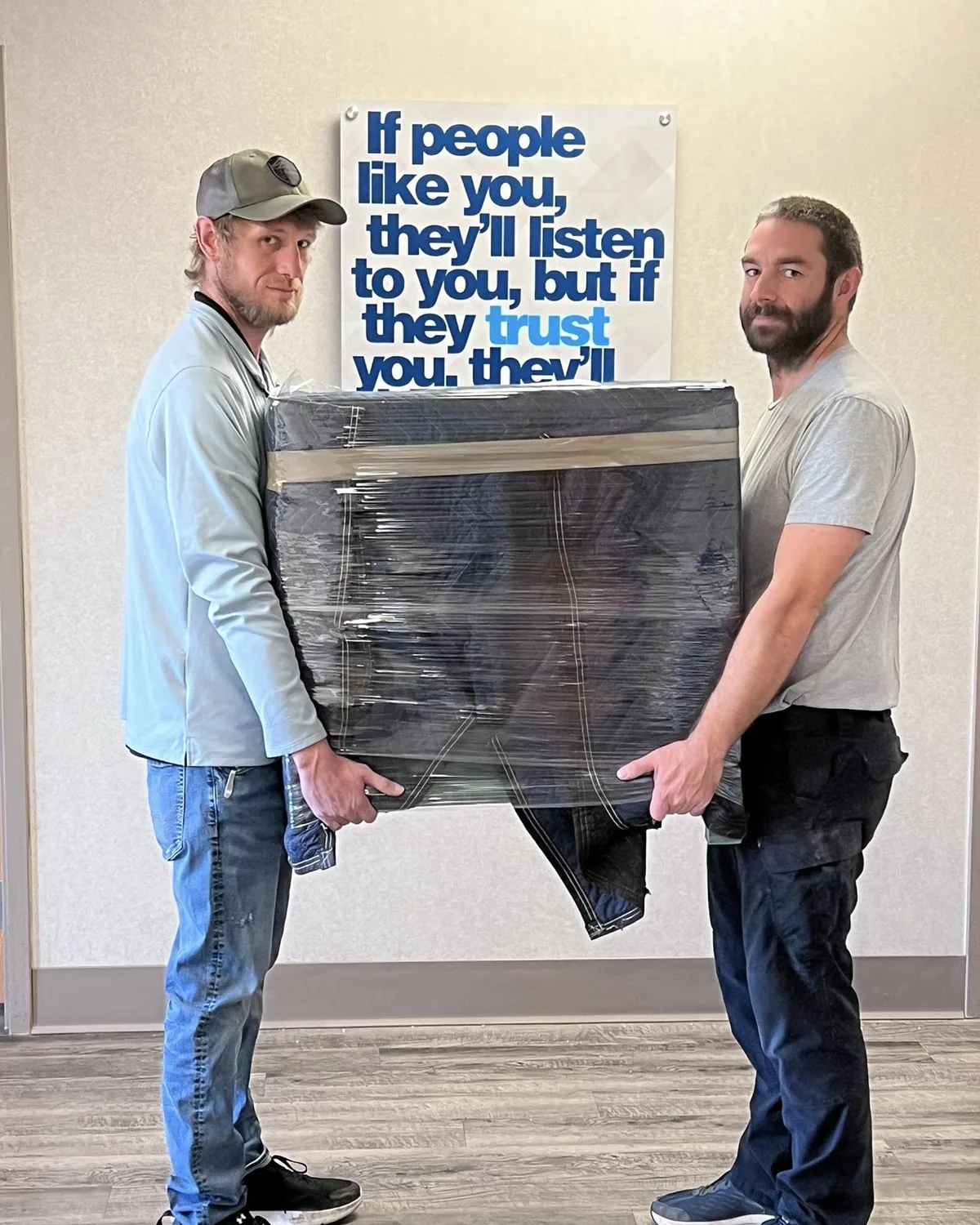 Shaun and Derek of Tullock Transport carrying a blanket-wrapped cabinet out of the office