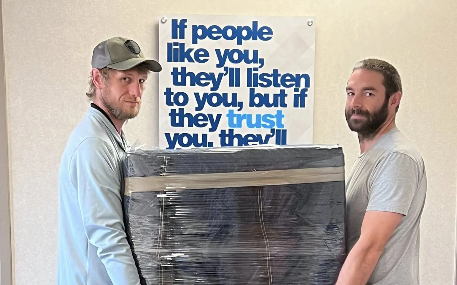 Shaun and Derek of Tullock Transport carrying a blanket-wrapped cabinet out of the office